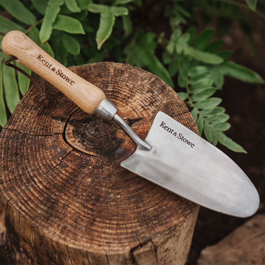 kent and stowe stainless steel hand trowel on a log